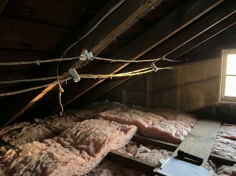 Aged knob-and-tube wiring with cracked insulation between attic joists posing a fire risk